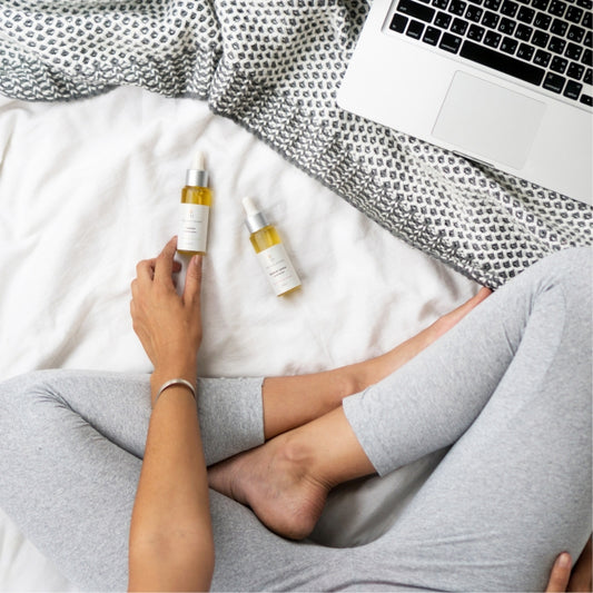 Original Human Co. Facial Serums - overhead shot of a woman sitting crosslegged on a bed with her computer and two bottles of Original Human Facial Serum in front of her.