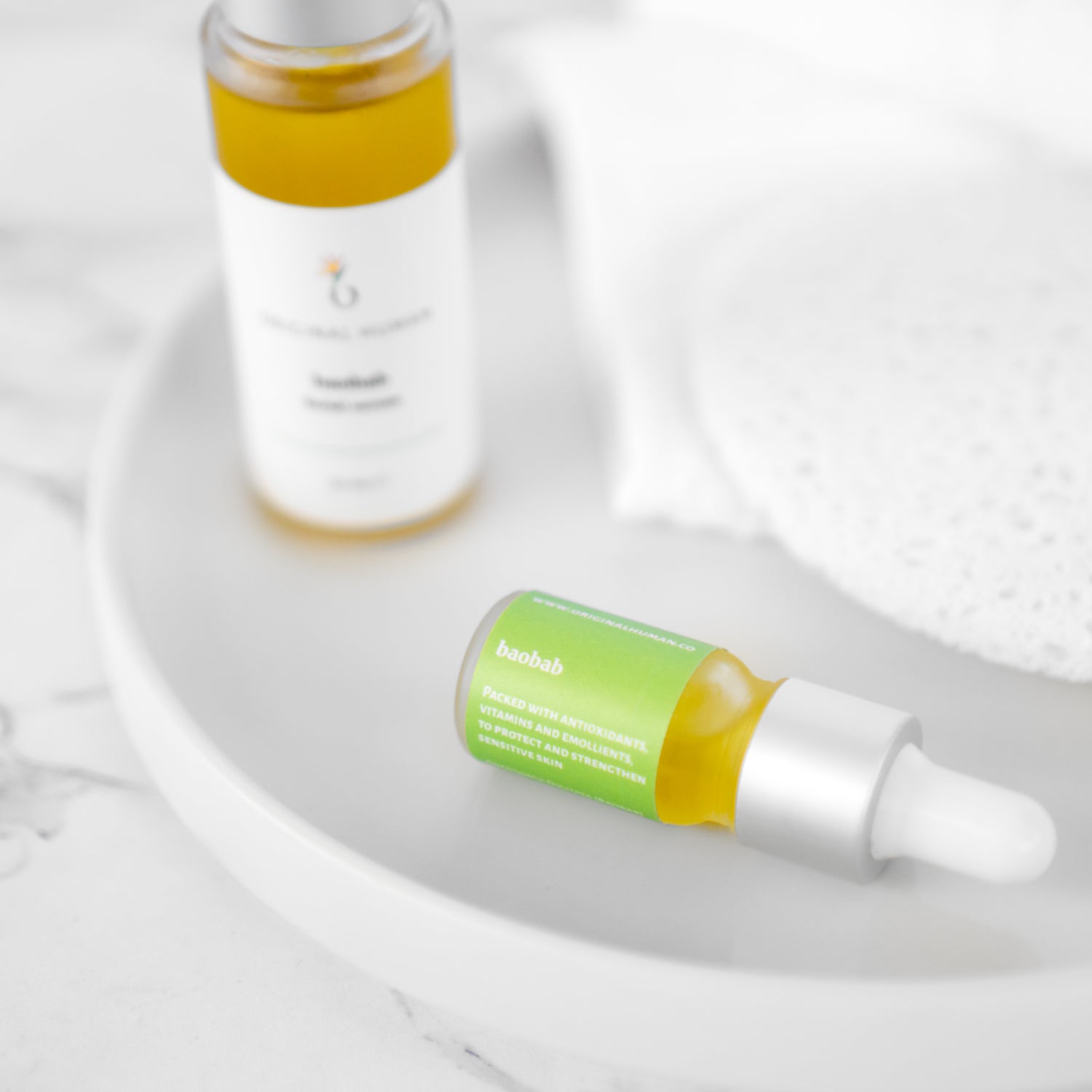 Original Human Co. Facial Serums, Baobab Facial Serum - close up shot of a sample bottle of Original Human Co. Baobab Facial Serum with a full bottle in the background.